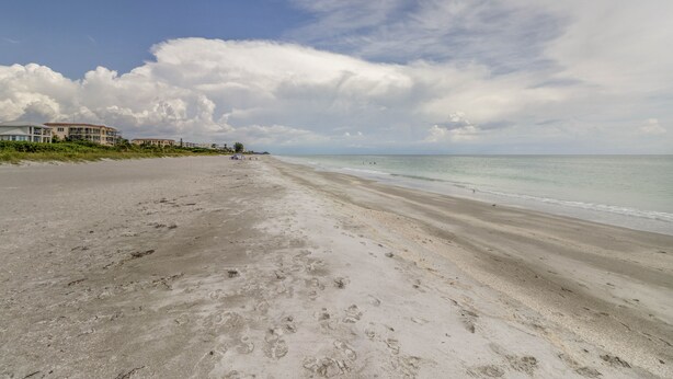 Une plage parsemée d’empreintes, un ciel dégagé et des bâtiments en arrière-plan.