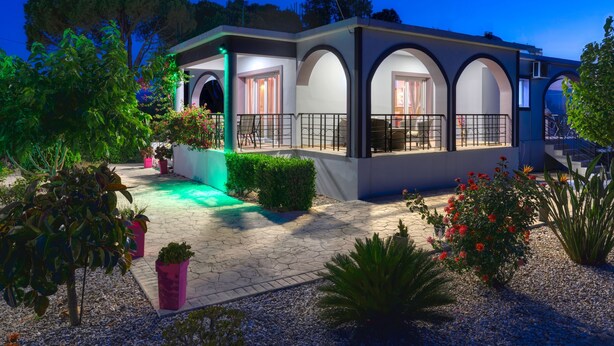 Uma casa moderna com varanda coberta, vasos de plantas e um jardim bem cuidado.