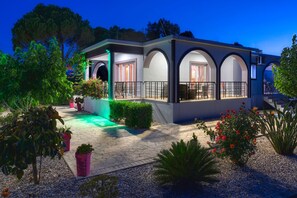 Una casa moderna con un porche cubierto, plantas en macetas y un jardín bien cuidado.
