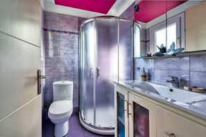 Un baño con cabina de ducha curva, inodoro y lavabo con espejo superior.