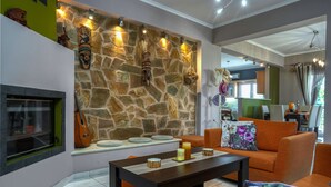 Sala de estar com parede de pedra, lareira, móveis laranja e mesa de jantar com velas.