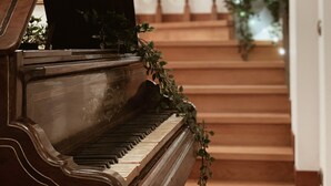 A grand piano with greenery on its keys, leading to a staircase with a railing decorated with plants.