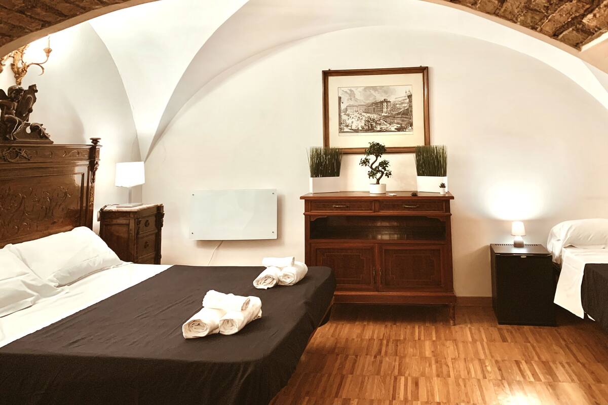 Ein Hotelzimmer mit Bett, Schreibtisch, Stuhl, Lampe, einem gerahmten Bild und einer Topfpflanze.