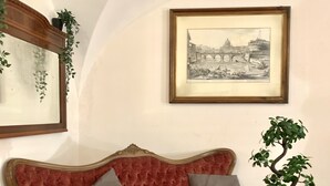 A room with a red velvet sofa, a round wooden table with a potted plant, and a framed picture on the wall.