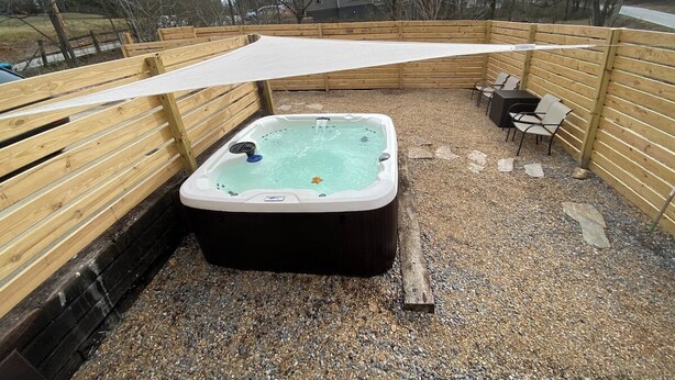 A hot tub in a fenced outdoor area with a wooden deck and chairs. - Asheville Rustic Cabin: Hot Tub, Pets ok, Fire Pit (Asheville)