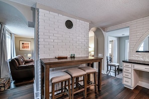 A kitchen with a white brick wall, wooden bar stools, and a dark wooden floor.