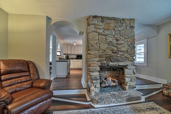 A living room with a stone fireplace, a leather sofa, and a kitchen in the background.