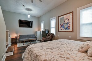 A bedroom with a large bed, a sofa, a chair, a TV, and artwork on the wall.