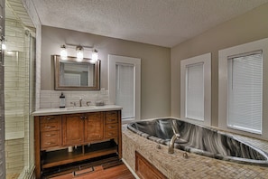 A bathroom with a large marble bathtub, wooden vanity, and a mirror with three lights.