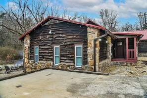 A rustic cabin with a stone foundation and wooden walls, featuring a red roof and a small porch area.