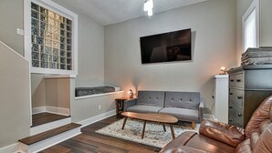 Un salon avec un canapé gris, un divan en cuir marron, une table basse en bois et un tapis à motifs.