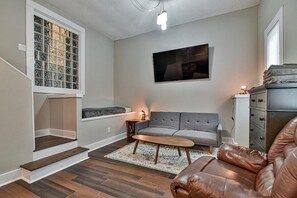 Een woonkamer met een grijze bank, een bruine leren hoekbank, een houten salontafel en een vloerkleed met een patroon.