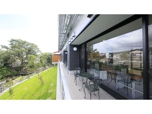 Un edificio moderno con un balcón que tiene mobiliario exterior y una pared de vidrio con vistas del entorno.