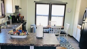 A kitchen with a central island, bar stools, a dining table with chairs, and a window with a view. - Lily’s Pad 5 minute drive from the Interlochen Arts accademy (Interlochen)