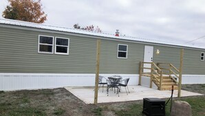 A single-story building with a patio area, a small table with chairs, and a wooden staircase leading to a door. - Lily’s Pad 5 minute drive from the Interlochen Arts accademy (Interlochen)