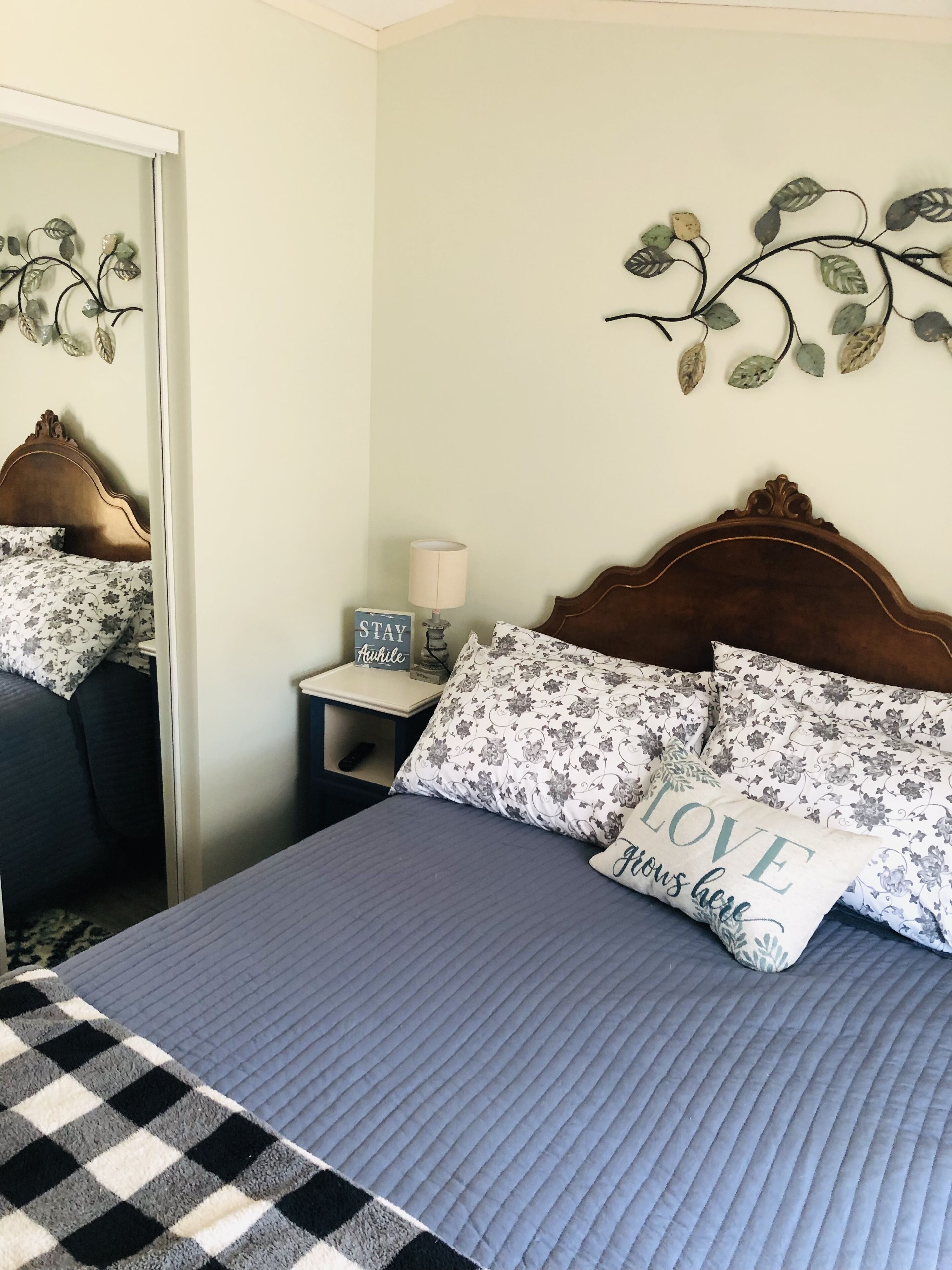 A neatly made bed with floral bedding, a checkered blanket, and decorative pillows.