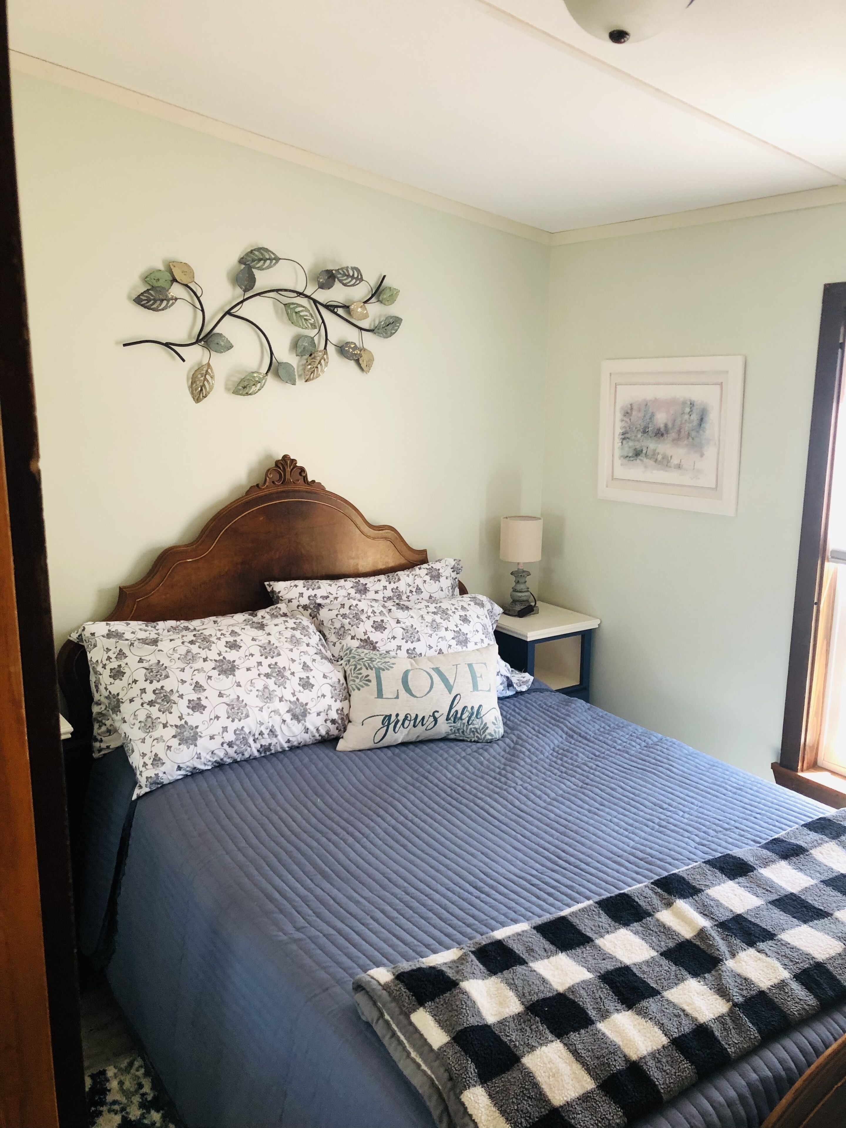 A neatly made bed with a blue quilt, a checkered throw blanket, and decorative pillows.