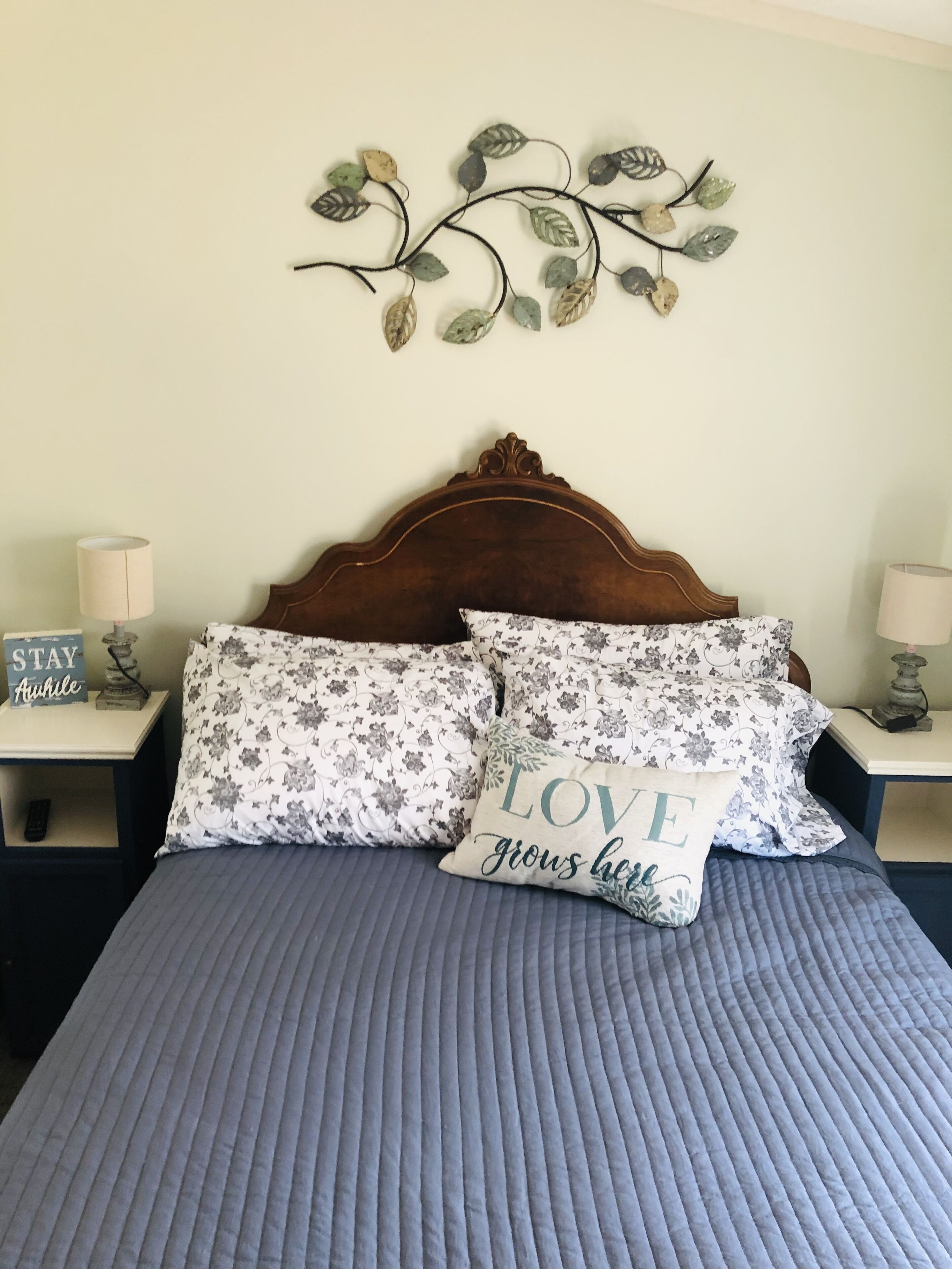 Un lit bien fait, recouvert d’une courtepointe bleue, agrémenté de deux coussins à motifs floraux et d’une décoration murale en forme de feuille.
