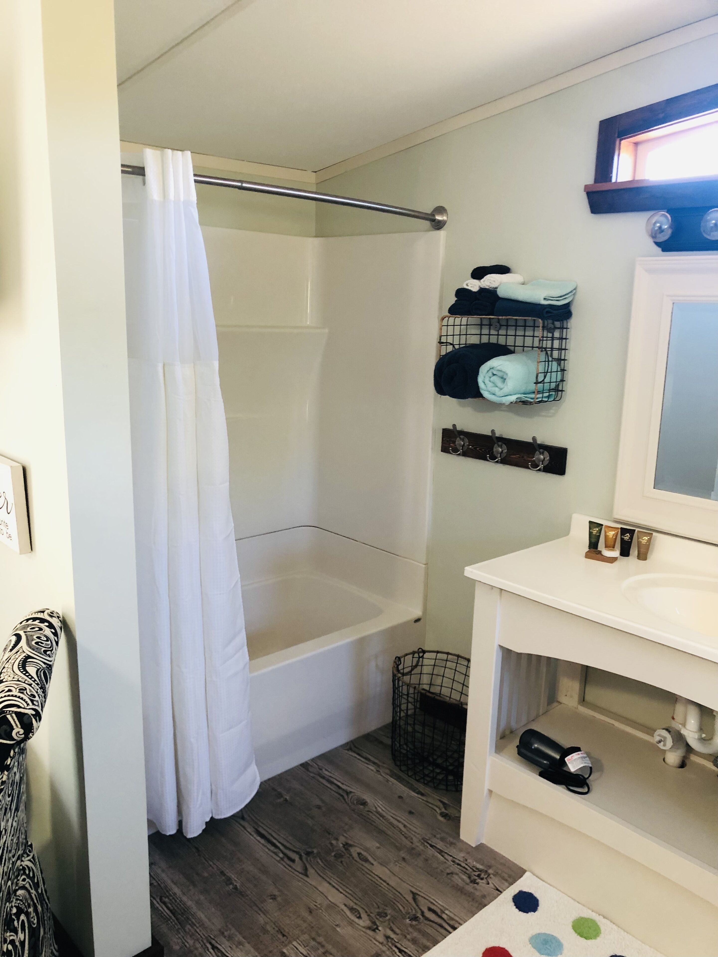Un baño con bañera, cortina de ducha, toallero con toallas, lavabo y espejo.