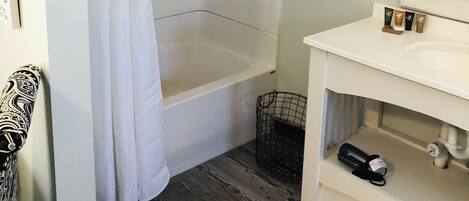 Un baño con bañera, cortina de ducha, toallero con toallas, lavabo y espejo.