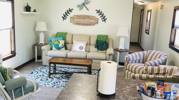 A living room with a sofa, coffee table, striped armchair, and a kitchen area with a marble countertop and a dish rack. - Lily’s Pad 5 minute drive from the Interlochen Arts accademy (Interlochen)