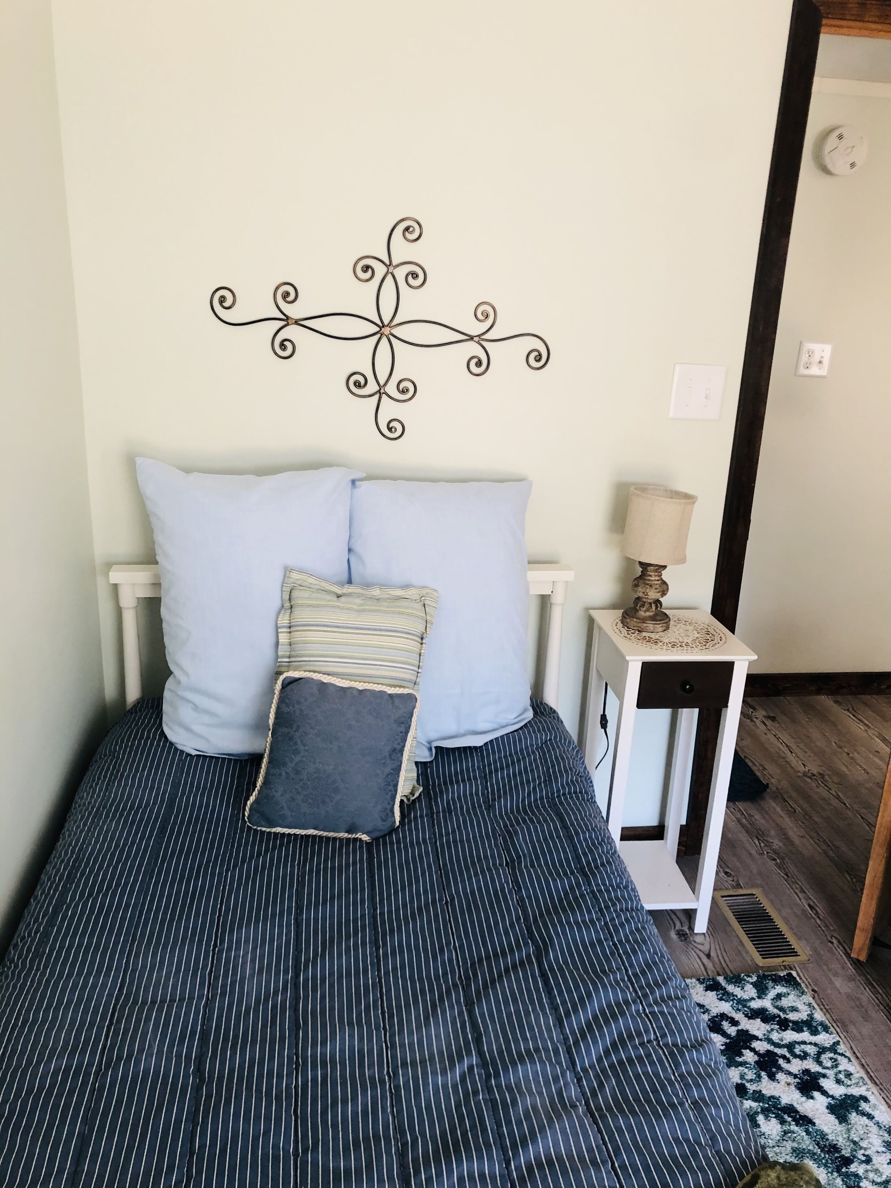 A bed with striped bedding, a decorative wall piece, a bedside lamp, and a patterned rug.
