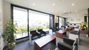 Relax in our spacious lounge area with large windows offering views of the surrounding area, sofas, chairs, and a flat-screen TV.