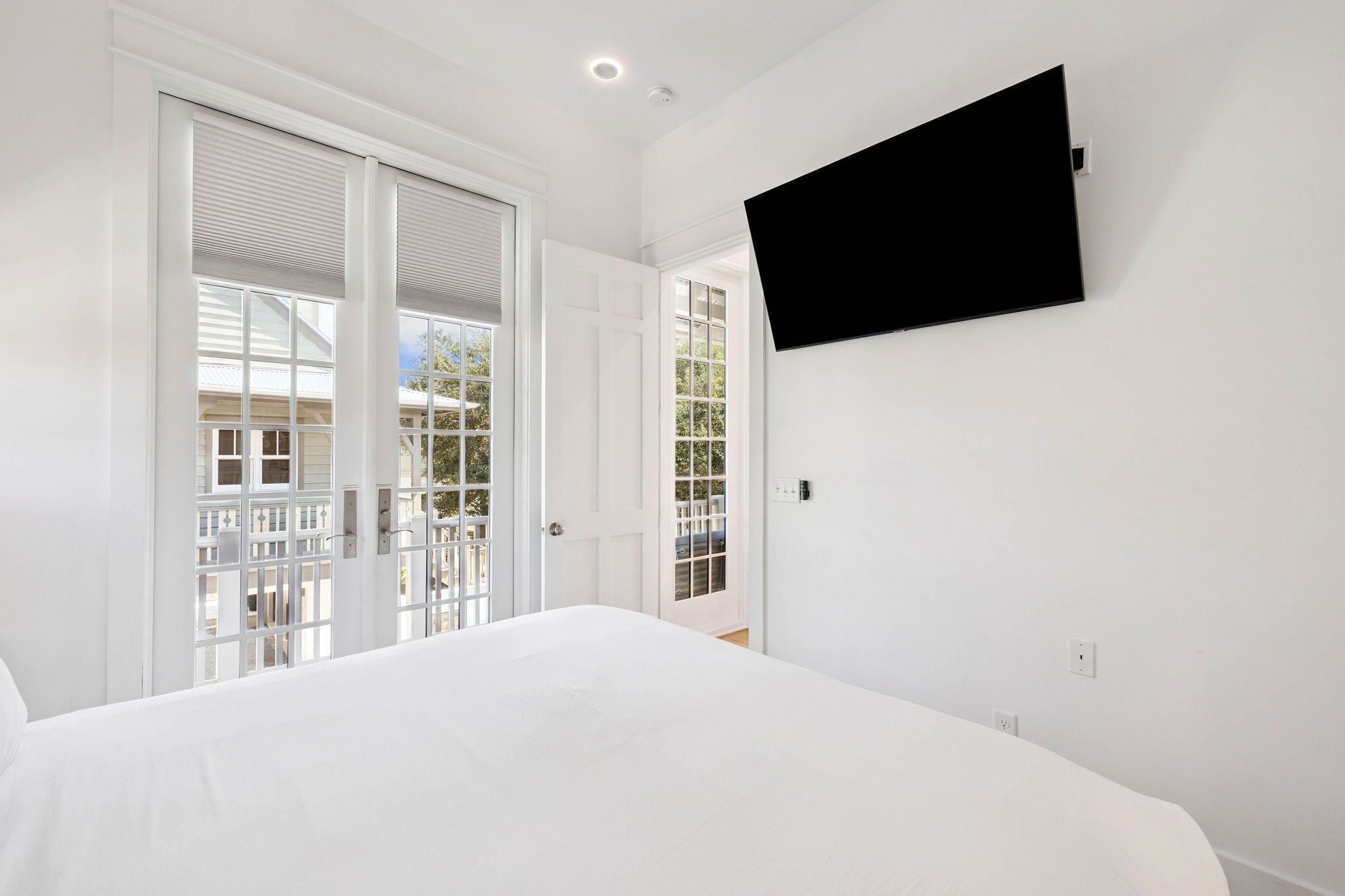Un dormitorio con cama, televisor montado en la pared y puerta corrediza de vidrio que da a un espacio exterior.