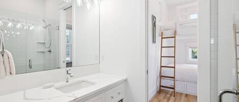 A modern bathroom with a large mirror, white vanity, and a shower area.