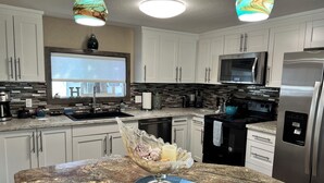 Una cocina moderna con armarios blancos, encimera de granito, refrigerador de acero inoxidable y un microondas.