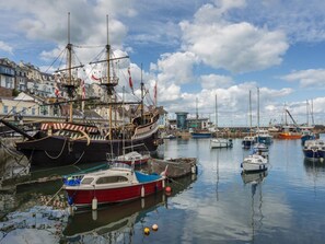 Ein Hafen mit verschiedenen Booten, darunter ein großes Schiff und kleinere Boote, die an der Kaimauer festgemacht sind.