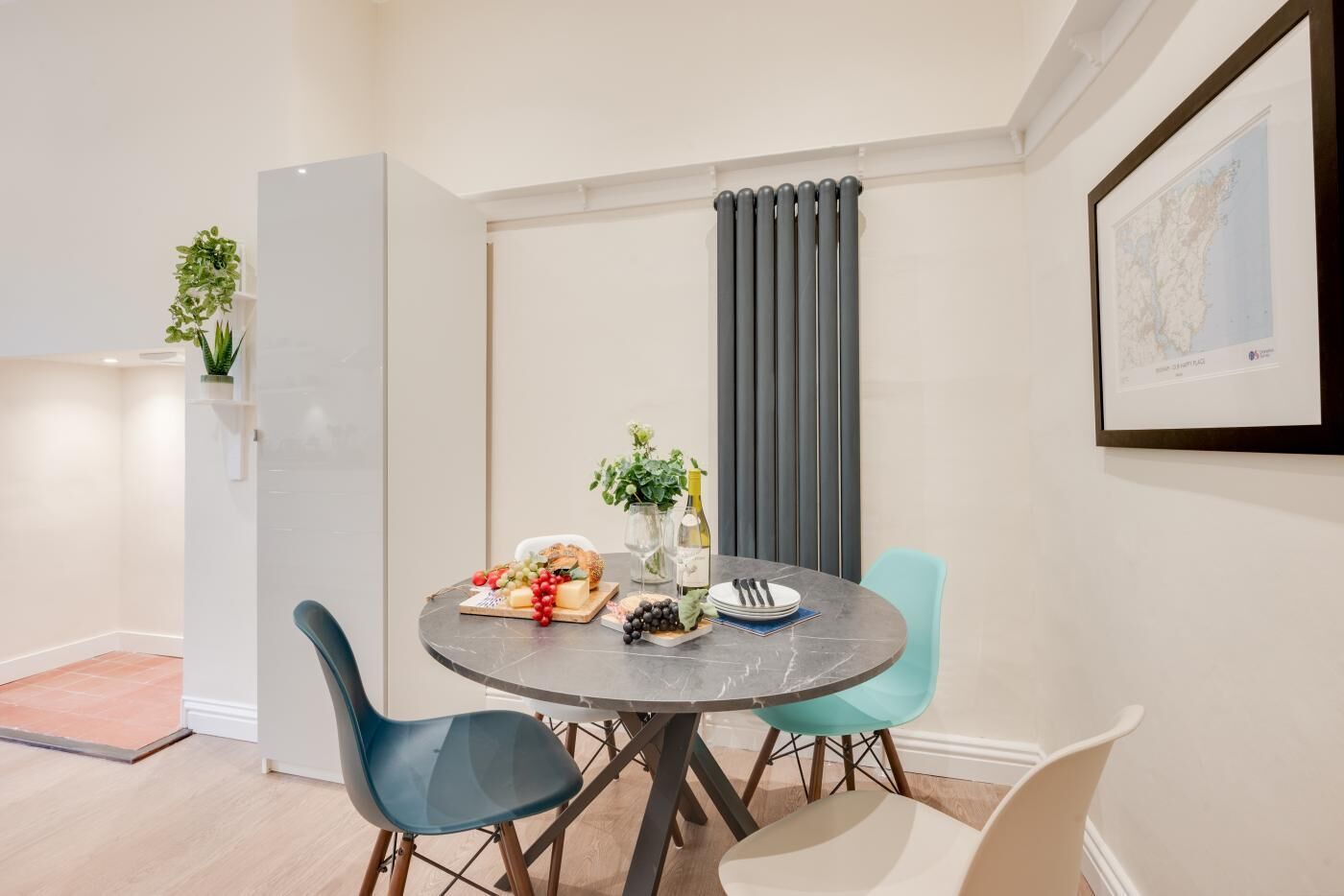 A dining area with a round table, chairs, a plant, and a framed map on the wall.