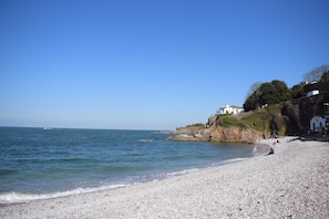 A pebble beach with a clear blue sky, calm sea, and a white building on a cliff. - 2 Bed in Brixham (oc-sdbolt) (Brixham)