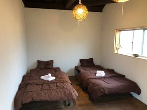 Two single beds with brown duvets and pillows, a window, and a unique light fixture.