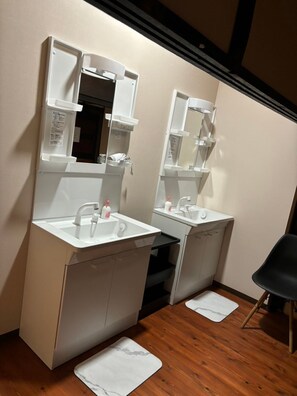 Bathroom features two sinks with chrome faucets and mirrors, a chair for seating, and wooden flooring.
