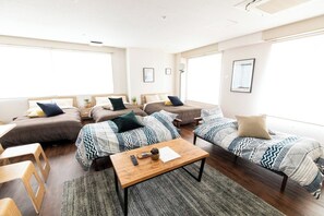 A spacious living area with multiple sofas and a coffee table, large windows providing natural light, and a minimalist decor style.