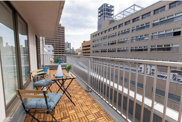 A balcony with wooden flooring, two folding chairs, a small table, and a potted plant.