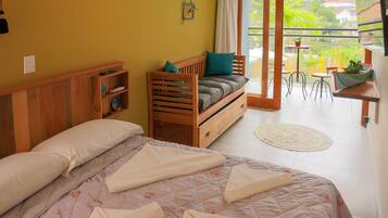 A bedroom with a large bed, a wooden bench, and a view of the outdoors through a sliding door.