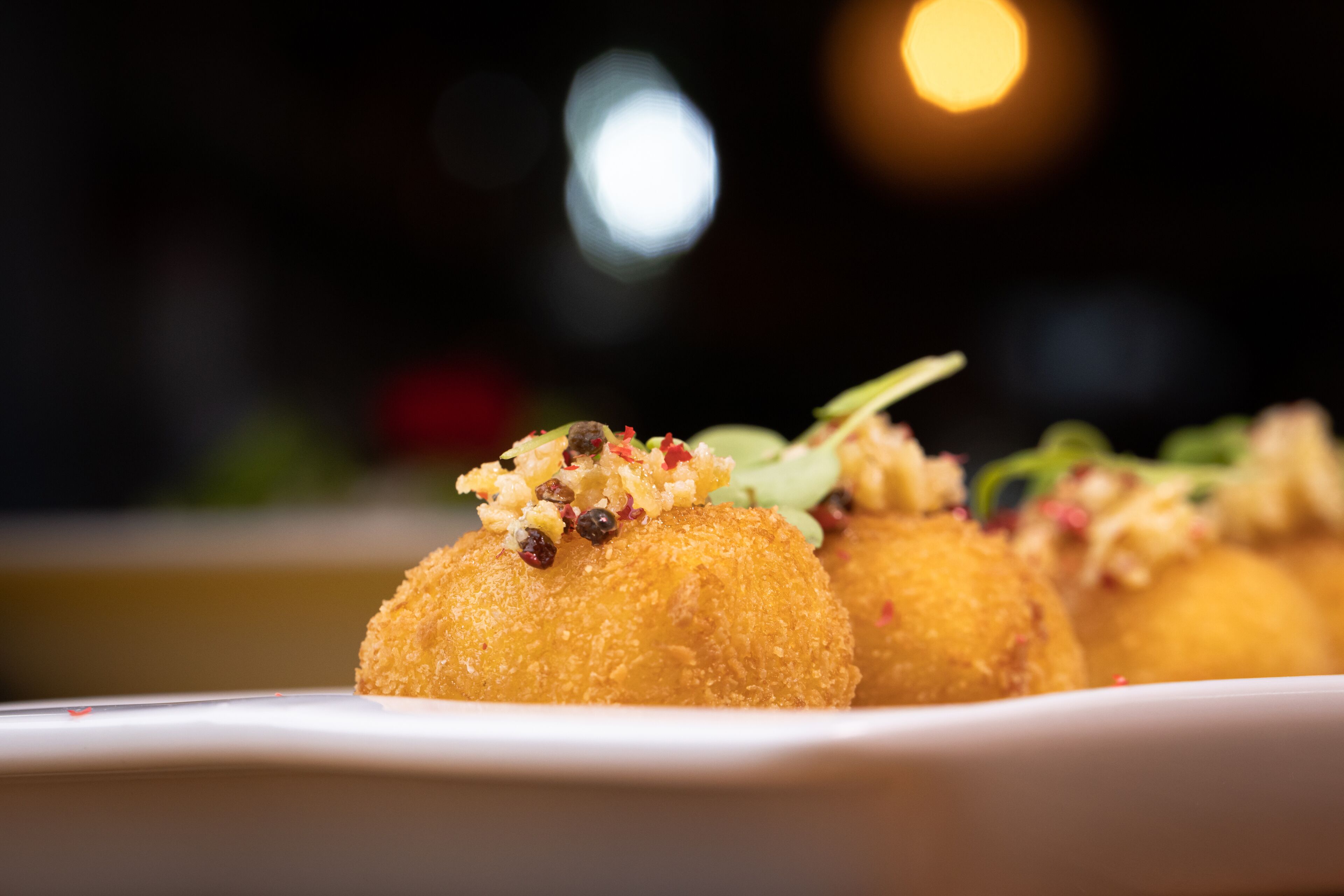Primer plano de tres croquetas doradas sobre un plato blanco, adornadas con hierbas y especias.