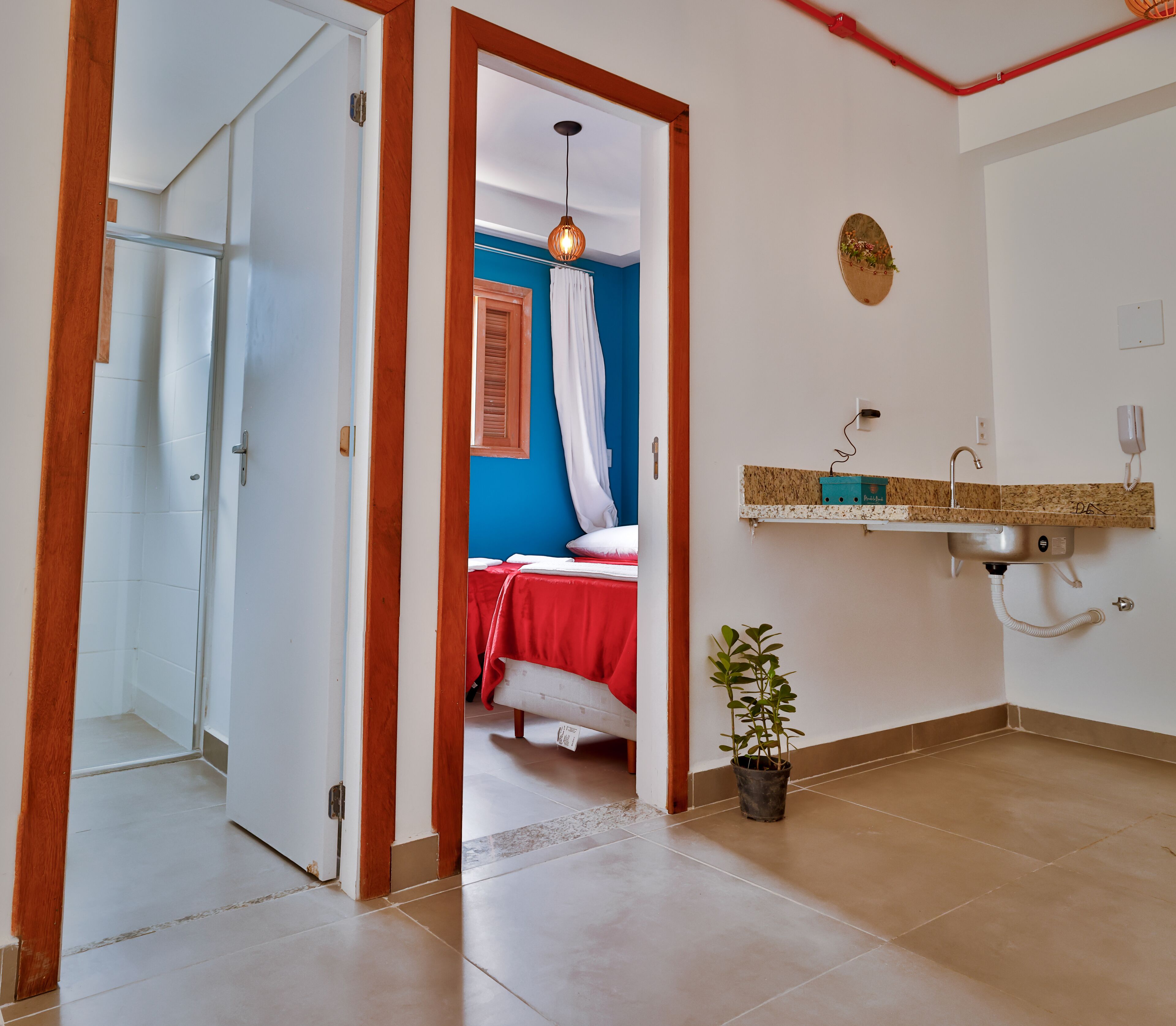 Een kamer met een bed, een wastafel, een plant in pot en een douche.