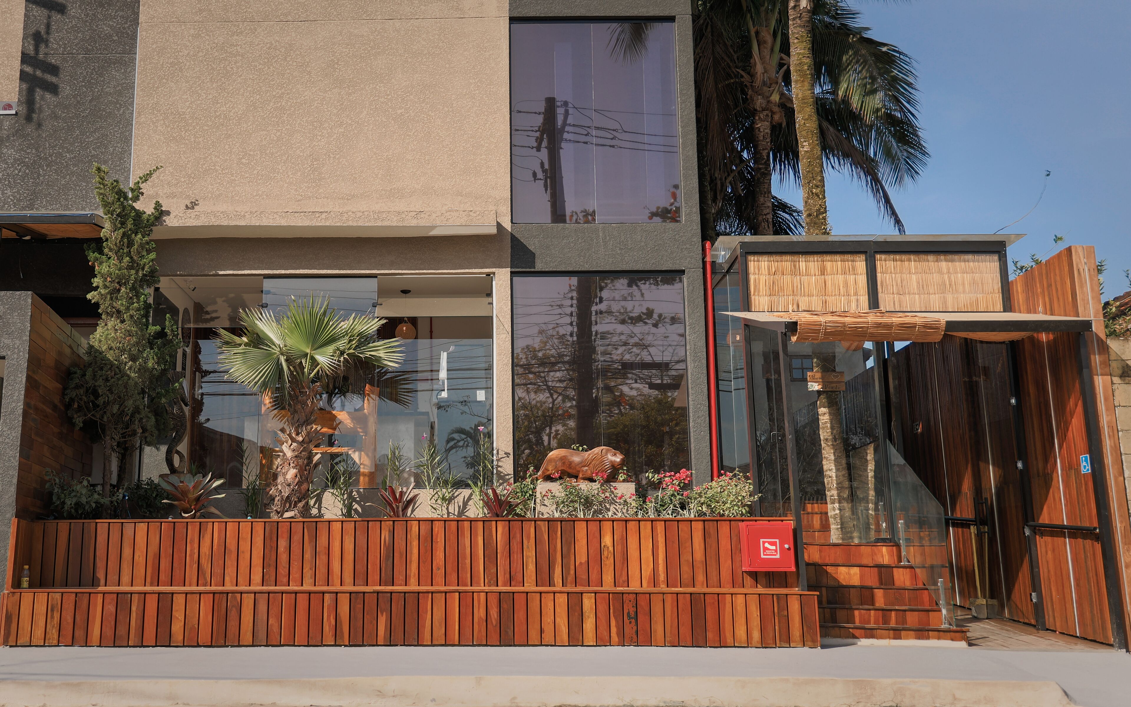 A modern building with a wooden fence, a glass entrance, and a small garden with plants and a wooden sculpture.