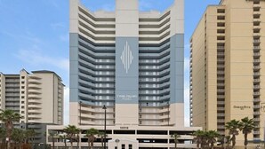 Un hotel de gran altura con diseño moderno, que presenta un logotipo destacado en la fachada, múltiples balcones y un garaje para coches en la base.