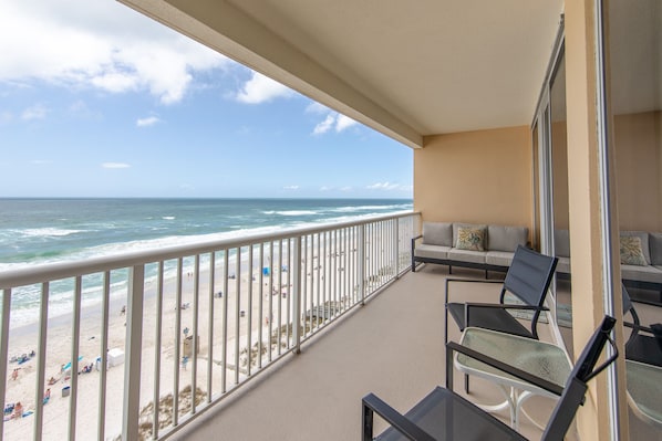 A balcony with a view of the beach and ocean. There are chairs and a table on the balcony.
