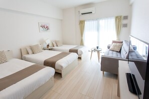 Quarto de hotel com duas camas, um sofá, uma TV e uma mesa pequena.
