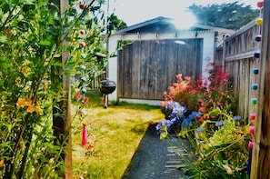 En trädgård med ett staket av trä, en grill och färgstarka blommor.
