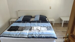 A neatly made bed with a striped bedspread, two pillows, and folded towels on a white headboard. - Kleines Ferienhaus im Zentrum von Bad Schandau (Bad Schandau)