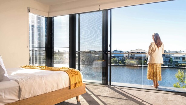 A bedroom with a large window, a bed, and a view of a body of water and buildings. - Luxury Lakeside Living at Birtinya (Birtinya)