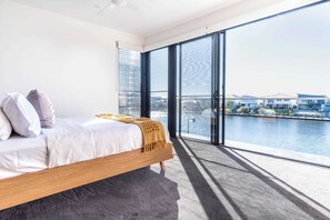 Un dormitorio con una ventana grande, una cama y vista a un cuerpo de agua.