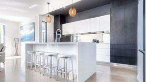 A modern kitchen with a central island, bar stools, pendant lighting, and a view of the city. - Luxury Lakeside Living at Birtinya (Birtinya)