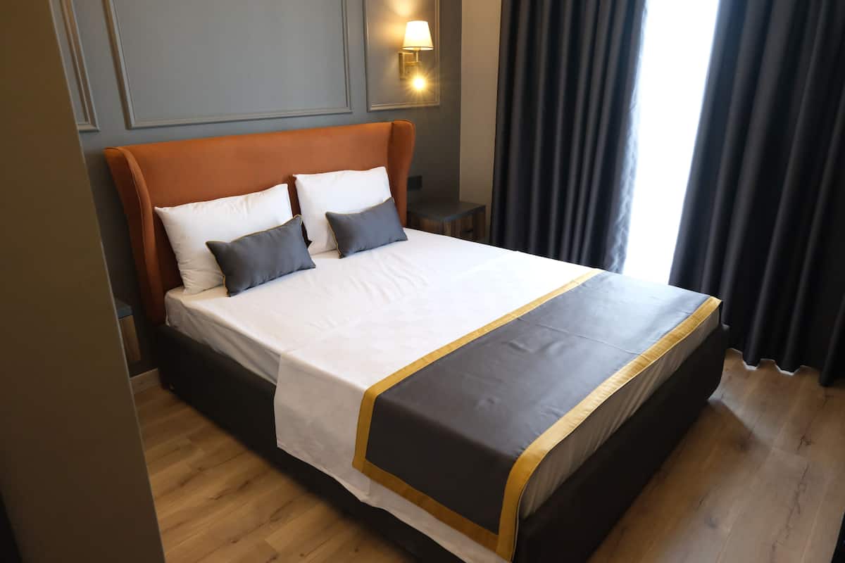 Una cama bien tendida con colcha blanca y negra, un cabecero de madera y una mesita de noche con una lámpara.